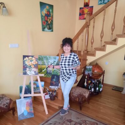 Maria Galuba z obrazem i pędzlem. W tle schody i obrazy