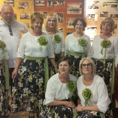 zespół pozuje do zdjęcia bobiety w białych koszulach i kolorowych spódnicach