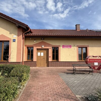 świetlica w Zimnej Wodzie z zewnątrz pomarańczowa z brązowym dachem. przed wejściem ławka.