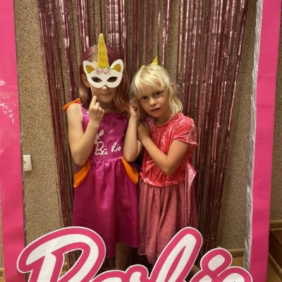 Zdjęcie przedstawia dwie dziewczynki pozujące w "kartonie lalki Barbie".