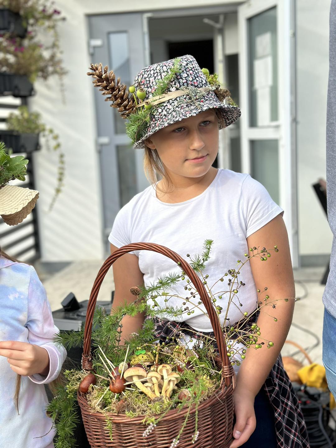 Na zdjęciu widzimy dziewczynkę, która ma kapelusz przyozdobiony "darami lasu" i koszyk "runo leśne".