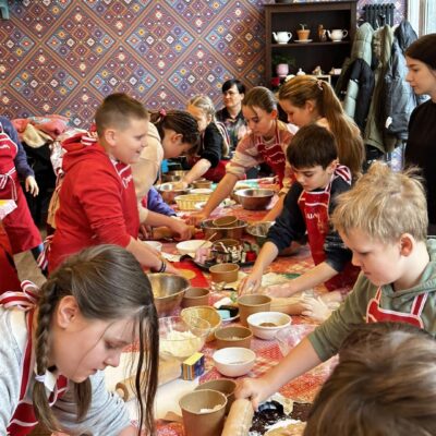 Grupa dzieci robiąca pizzę na warsztatach kulinarnych.