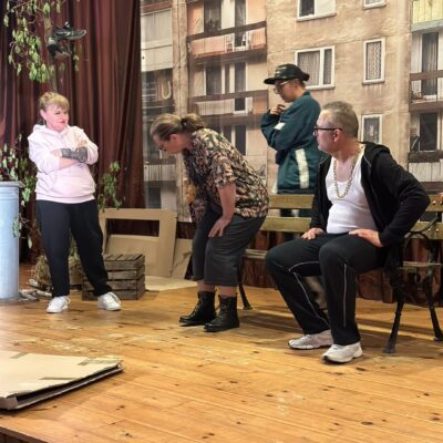 Aktorzy na scenie siedzą na ławce.