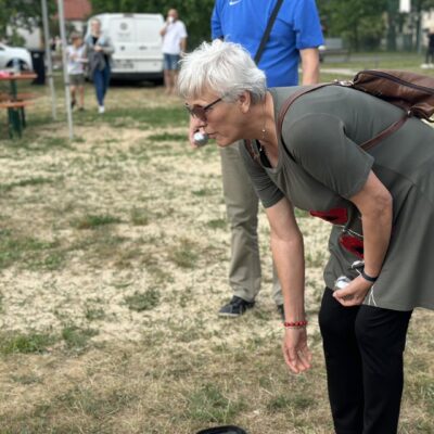 Seniorka pochyla się podczas gry w bule, oddajac rzut.