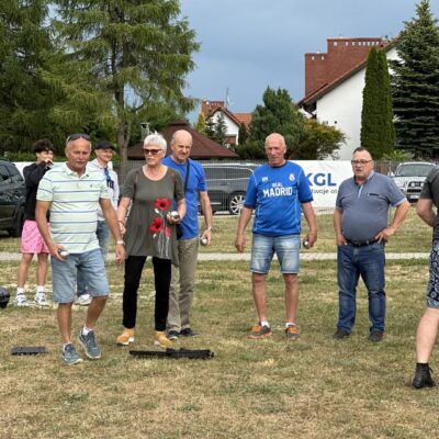 Seniorzy grają w bule na trawie.