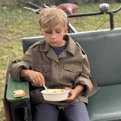 Chłopiec w stroju wojskowym je grochówkę