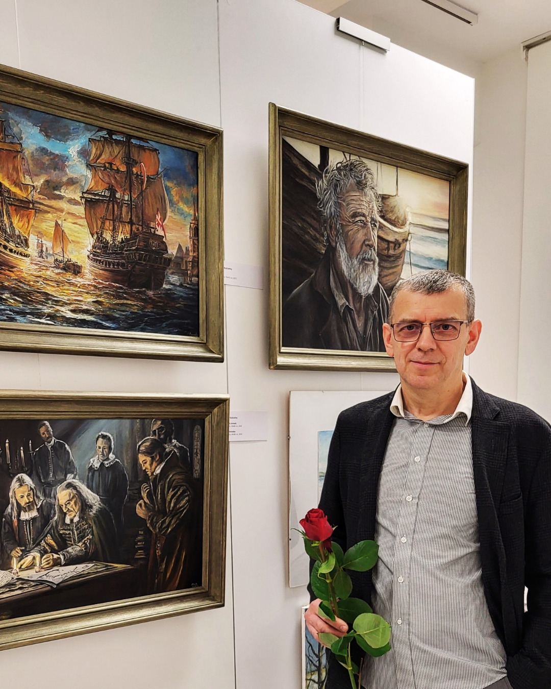 Jarosław Kościelny z różą w ręku, na tle swoich obrazów