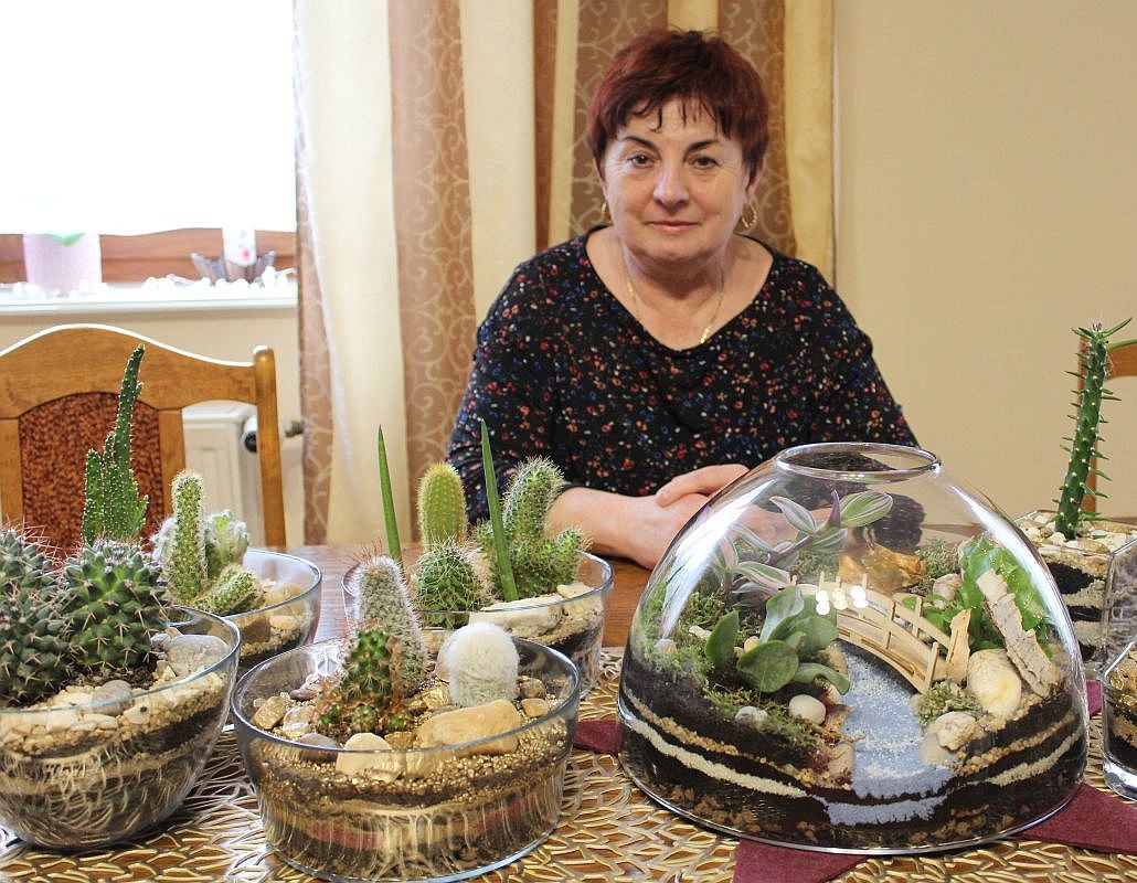 Urszula Kurowska siedząca przy stole ze swoimi pracami