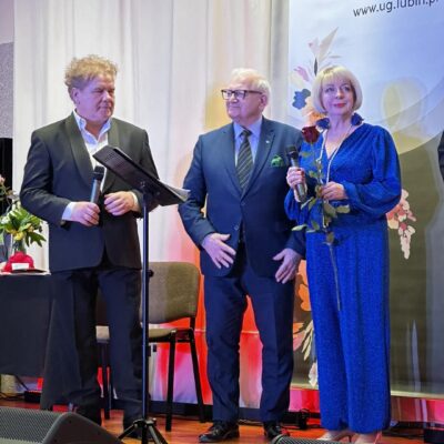 Podziękowania na scenie dla artystów. Mężczyźni wręczają kobiecie kwiaty.