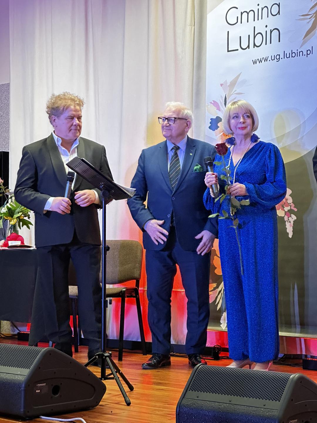 Podziękowania na scenie dla artystów. Mężczyźni wręczają kobiecie kwiaty.