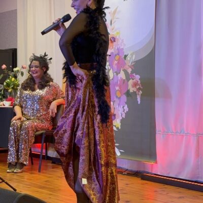 Kobieta tańczy i śpiewa na scenie w złoto czarnej sukni.