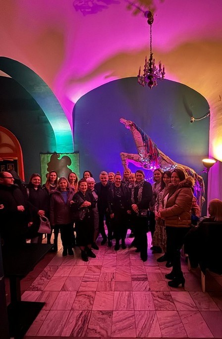 Wspólne zdjęcie uczestników spotkania w wysokim pomieszczeniu z dużą wiszącą lampą.