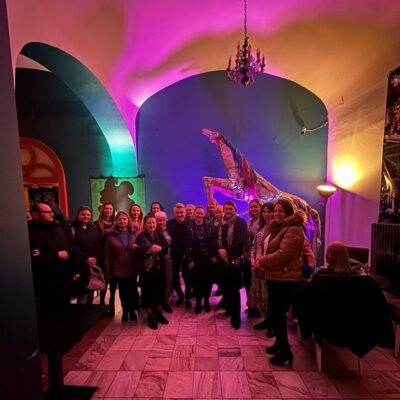 Wspólne zdjęcie uczestników spotkania w wysokim pomieszczeniu z dużą wiszącą lampą.