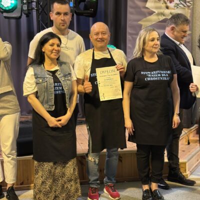 Pan z dyplomem pod sceną oraz dwie kobiety po bokach.