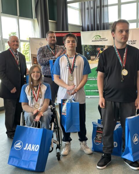 Nagrodzeni zawodnicy z medalami. Trzech mężczyzn i dziewczyna na wózku inwalidzki. 
