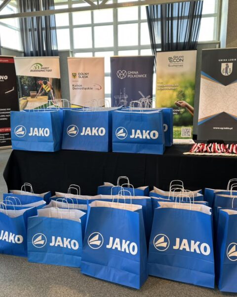 Nagrody w dużych niebieskich torbach oraz puchary i medale. w tle banery sponsorow