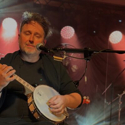 Jeden z członków zespołu gra na banjo, ma zamknięte oczy.