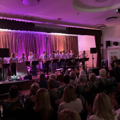 Zespół na scenie śpiewa.Kobiety w białych koszulach i spódnicach.