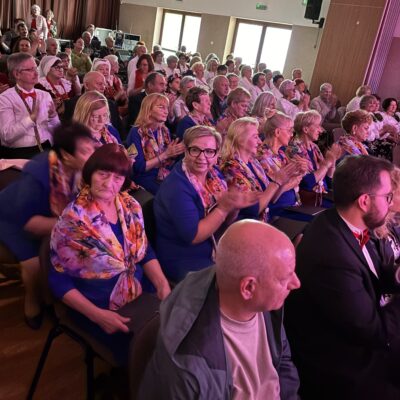 Chór na widowni w niebieskich sukienkach i kolorowych chustach