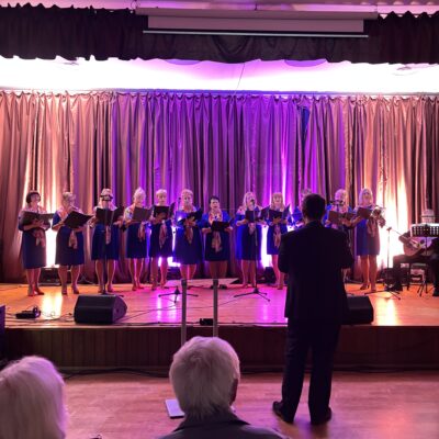 Chór na scenie z dyrygentem na pierwszym planie.