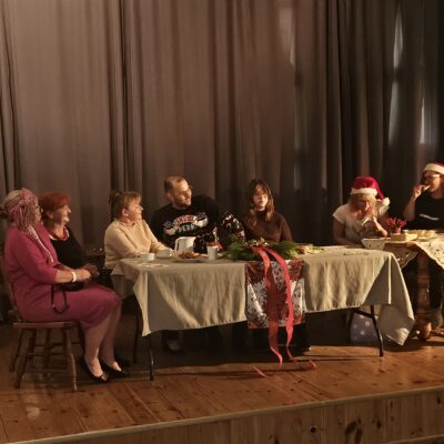 aktorzy przy stole na scenie siedzą i rozmawiają