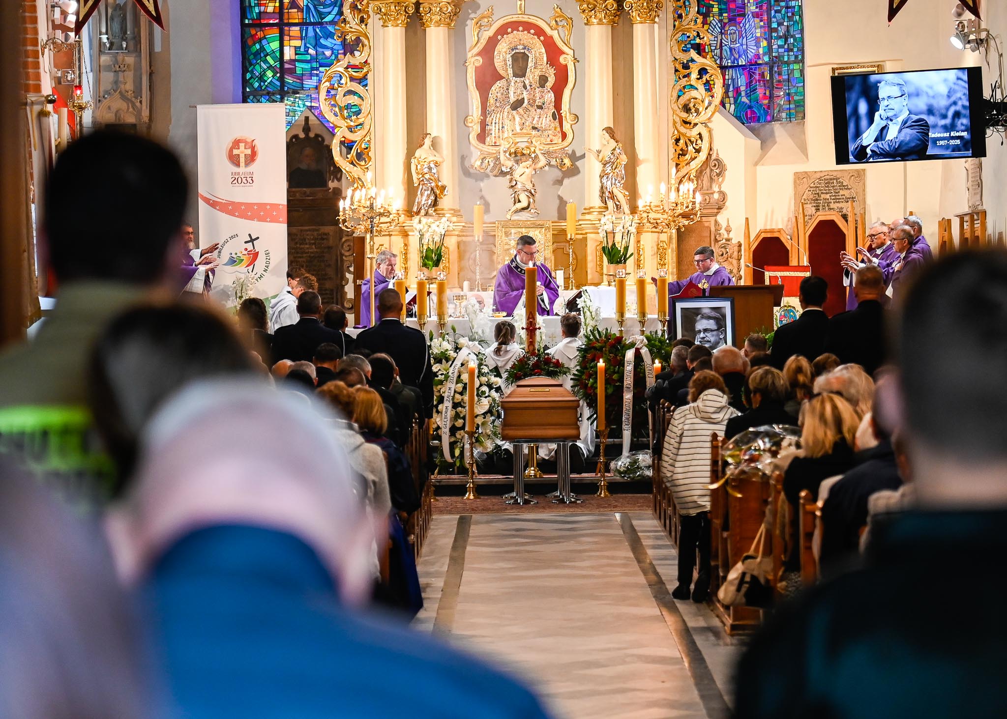 Ksiądz na ołtarzu, przed nim trumna. W ławkach zebrani ludzie.