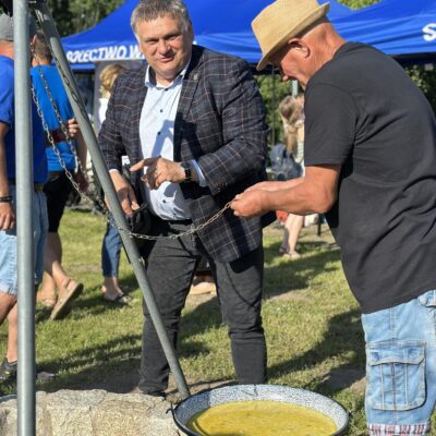 Radny Norbert Grabowski wraz z sołtysem stoi przy kotle z zupą i palenisku.