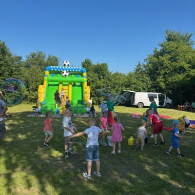 Dzieci bawią się bańkami, dmuchaniec w tle.