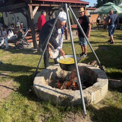 Radny Norbert Grabowski miesza zupę nad paleniskiem.