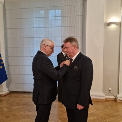 Tadeusz Kielan dostaje odznakę. W tle flaga Polski i Unii Europejskiej