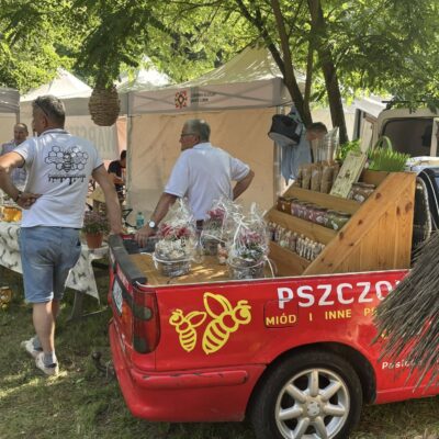 auto pszczelarza z miodami na pace, w tle jego stoisko