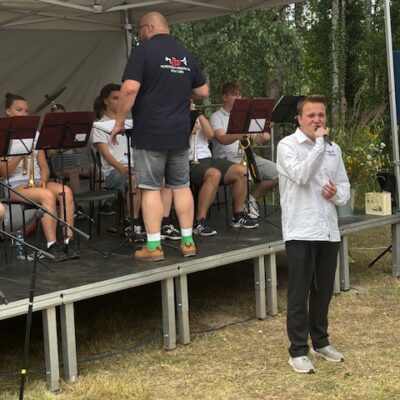 orkiestra na scenie gra na instrumentach dętych chłopak śpiewa przed sceną