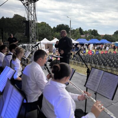 orkiestra na scenie na krzesłach z instrumentami w tle kapelmistrz