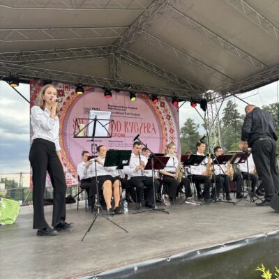 na scenie orkiestra dęta jedna kobieta spiewa