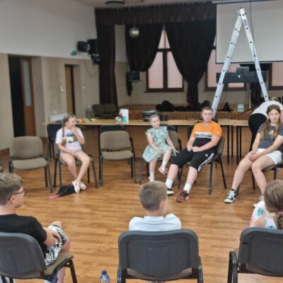 grupa dzieci siedząca na krzesłach w kręgu z instruktorem muzycznym