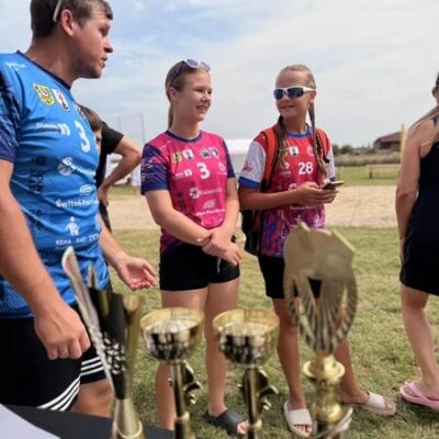 mężczyzna z dwiema dziewczynami w sportowych strojach, puchary na pierwszym planie