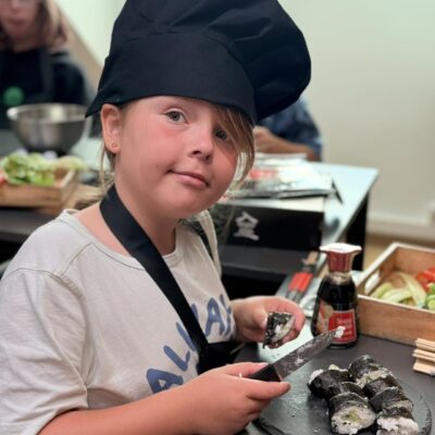 dziewczynka w czapce i fartuchu kroi sushi