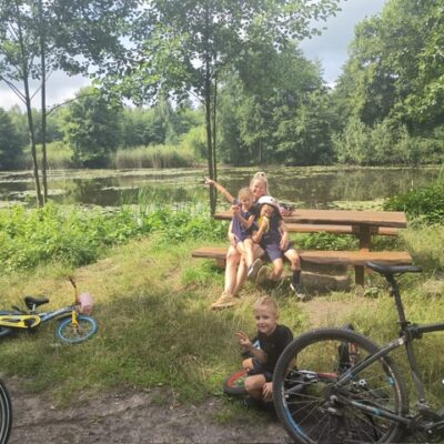 uczestnicy rajdu kobieta i dzieci odpoczywają na trasie w tle woda, rowery leżą obok
