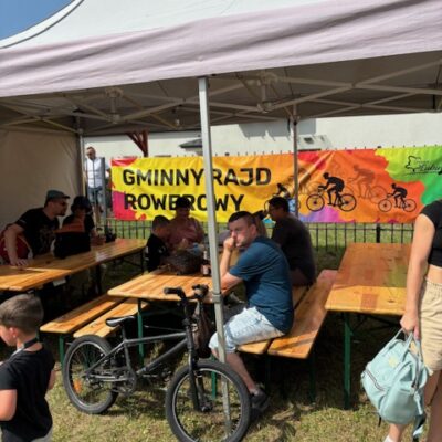 Rower opart o namiot przy ławkach ludzie w tle napis rajd rowerowy