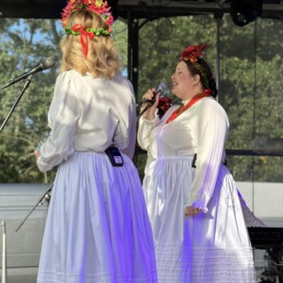 kobieta śpiewa do mikrofonu w pięknej sukni i czerwonych koralach