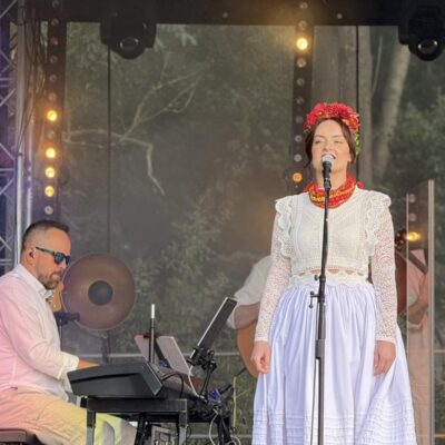 kobieta śpiewa do mikrofonu w pięknej sukni i czerwonych koralach