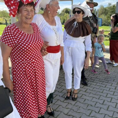 Osieczanki w przebraniach przed występem, czerwona suknia w grochy białe na kobiecie i kapelusz