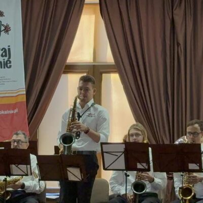 Mężczyzna z saksofonem na scenie w tle inni muzycy