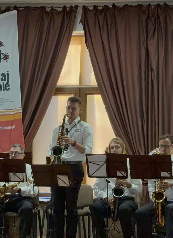 Mężczyzna z saksofonem na scenie w tle inni muzycy